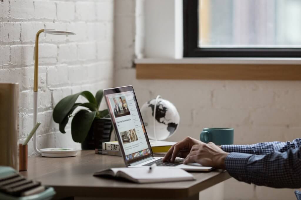 A person’s hands on a laptop on a wooden desk.