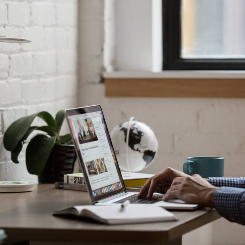A person’s hands on a laptop on a wooden desk.